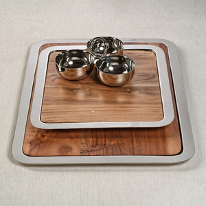 The BRASSERIE STEEL & ACACIA GASTRONOMY BOARD by ZODAX is a rectangular tray featuring a shiny metallic border and a wooden base. The acacia surface shows natural grains and knots, giving it a rustic appearance. With dimensions of 14.25 in x 12.25 in x .75 in, the tray rests on a white background.