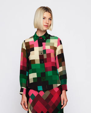 A woman with short blonde hair is wearing the MIRTO 1956 - MULTICOLOR SILK PLAID BLOUSE paired with a matching skirt. The chic fashion outfit from MIRTO 1956 features a collar and buttons down the front, showcasing green, pink, black, and brown squares on a white background.