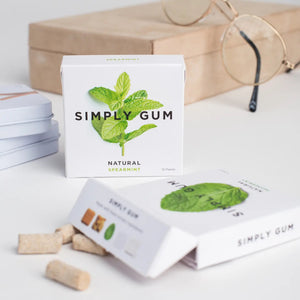 A white package of SIMPLY GUM - SPEARMINT NATURAL CHEWING GUM by SIMPLY GUM, featuring an image of fresh mint leaves. The gum, made with organic ingredients and free from aspartame, comes in a pack of 15 pieces with the text "CHEW BETTER" printed at the bottom.