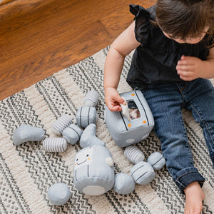 Description: Meet the TOT BOT from WONDER AND WISE ASWEETS, an educational toy designed to delight and educate. With its light gray body, segmented arms and legs, and cheerful yellow accents, this plush robot is sure to captivate. The friendly face sports black eyes and a happy smile, while the rectangular torso is adorned with colorful buttons and charming striped patterns on its limbs.