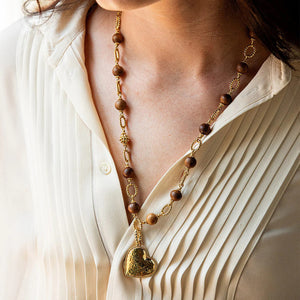 The CAPUCINE DE WULF - EARTH GODDESS LINK NECKLACE WITH TEAK by CAPUCINE DE WULF features alternating brown teak beads and intricate gold chain links. This versatile piece of jewelry is finished with a decorative gold clasp, giving it a sophisticated and elegant look.