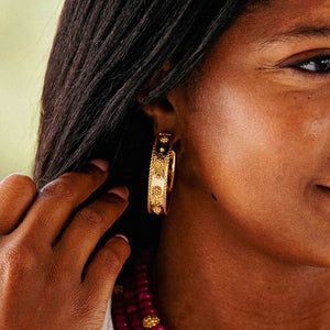 The CAPUCINE DE WULF - BERRY CLASSIC LARGE HOOP EARRINGS are 18K gold hoops featuring intricately detailed floral patterns with raised flowers arranged in a row, complemented by a polished finish that captures the light beautifully.