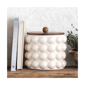 The CREATIVE COOP CANISTER WITH RAISED DOTS & ACACIA LID is an elegant piece featuring a white stoneware design with a circular pattern of raised bubbles. It has an acacia wood lid topped with a small, round wooden handle, making it perfect for stylish kitchen storage.