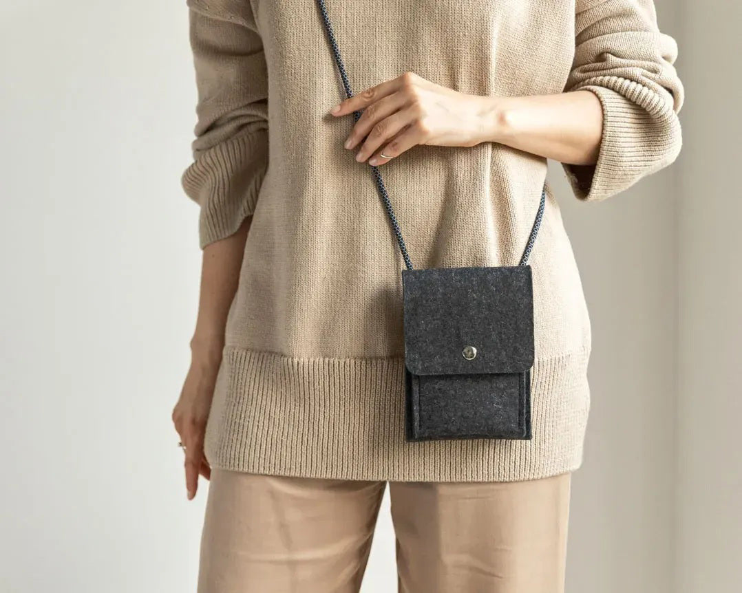 A person in a loose gray shirt and taupe pants carries the WOOLBERRY WOOL FELT PHONE BAG—a pink crossbody with a flap and silver chain—over their shoulder, showing only their torso and part of their arms.