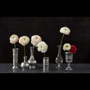 The MATCH - PEWTER BUD VASE by MATCH is a silver, round-bottomed vase with a narrow cylindrical neck, wide body, engraved lines, and dotted patterns around its midsection and shoulder, shown against a white background.