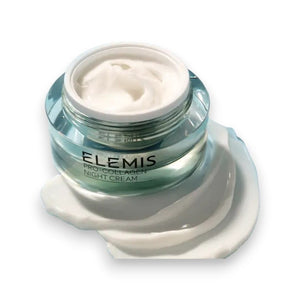 A clear, open jar of ELEMIS Pro-Collagen Night Cream 50ml from ELEMIS - STEINER, filled with white cream, rests on a puddle of spilled cream. The jar showcases a white label with the product name in black text. Perfect for achieving a radiant complexion, this night cream supports your anti-aging skincare routine. The background is white.