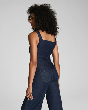 A woman with curly hair models the SPANX DENIM TAILORED VEST, posing confidently against a plain light gray background.