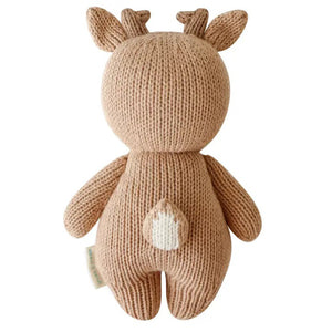 The CUDDLE + KIND - HANDMADE BABY FAWN by CUDDLE & KIND is a charming hand-knit baby fawn plush toy. It resembles a brown deer with two small antlers, round ears, and a petite white tail. The toy stands upright on its legs, facing backwards, highlighting its intricate stitching and soft texture—ideal for fair trade income newborn gifts.