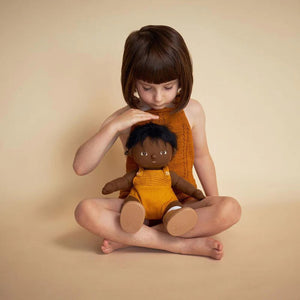 A DINKUM DOLL from OLLI ELLA USA features soft brown hair and comes dressed in a white knit romper paired with brown shoes. This charming doll has an embroidered face with brown eyes, a small nose, and a gentle smile. Its posable body makes it perfect for imaginative playtime, and it is posed standing upright.