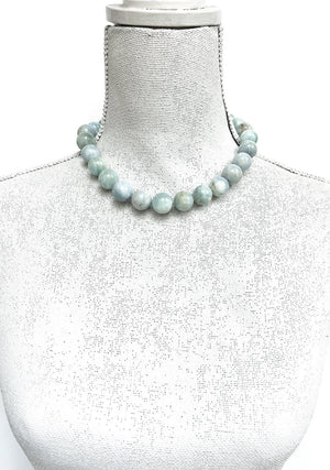 The ANN LIGHTFOOT - AQUAMARINE RAS DU COU NECKLACE is a breathtaking piece featuring large, round, polished beads in varying shades of light blue and green. The beads are intricately strung together and secured with a sterling silver clasp at the back. Arranged beautifully on a white background, this necklace offers an adjustable length for versatile wear.