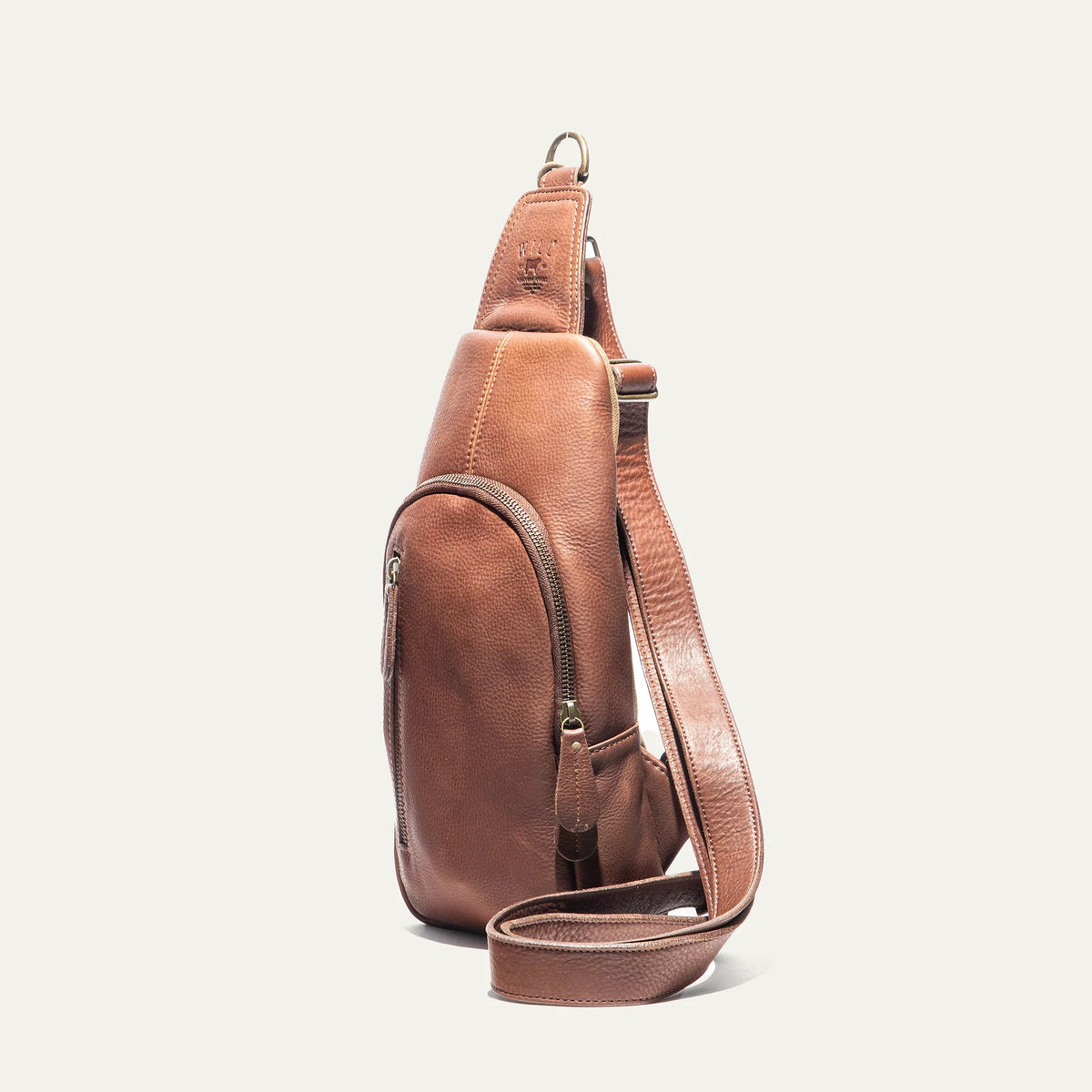 The WILL LEATHER GOODS - ZIP AROUND SLING BAG by WILL LEATHER GOODS is a brown full-grain leather sling bag with a zippered design, front zipper pocket, adjustable strap, and visible stitching, displayed upright on a white background.