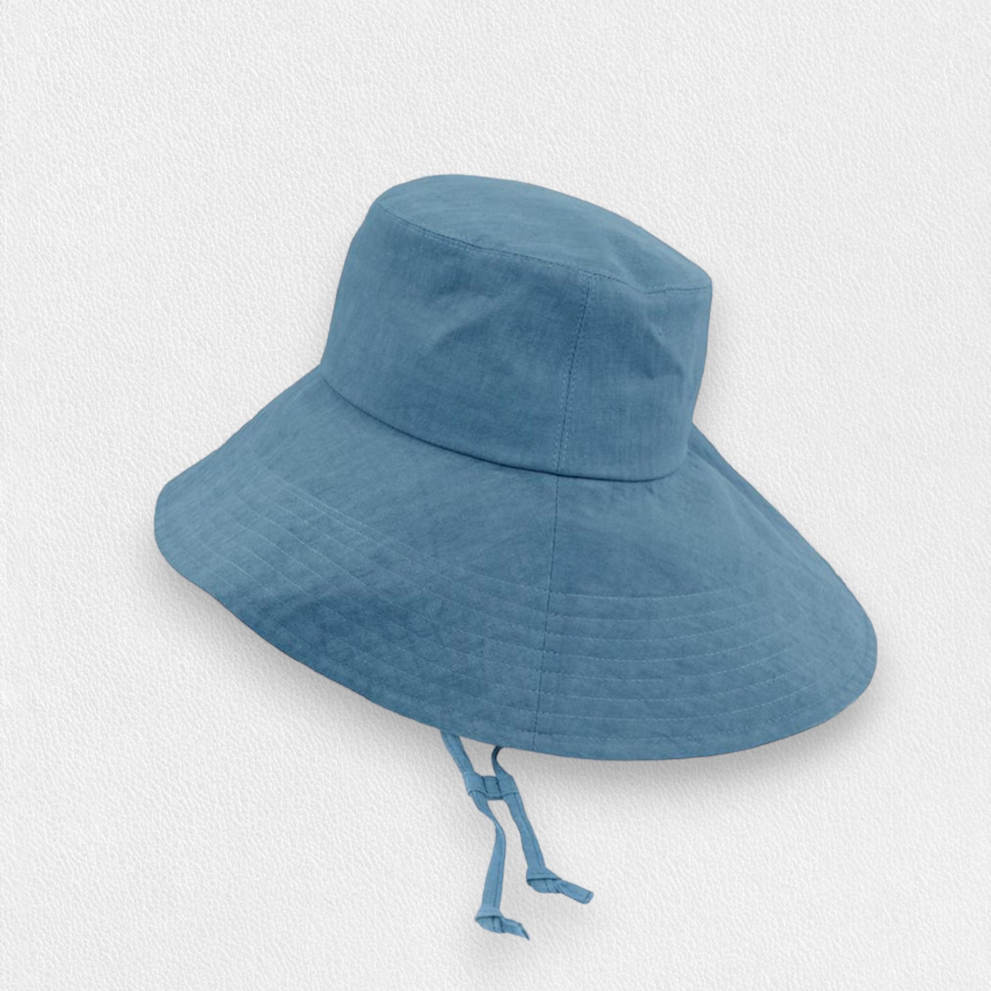 The FLAMINGO LINEN WIDE BRIM UV PROTECTION HAT features a light blue design with a wide brim and adjustable chin strap. Made from lightweight, UV-resistant fabric, it provides excellent sun protection. The hat is showcased against a plain, light-colored background.