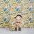 An OLLI ELLA USA DINKUM DOLL from the Pretend Pack Travel Sets, outfitted in a wide-brimmed hat, khaki overalls, and brown boots, poses with a petite suitcase. The backdrop showcases a vibrant, abstract pattern filled with diverse shapes and pastel hues, perfect for sparking endless imaginative adventures.