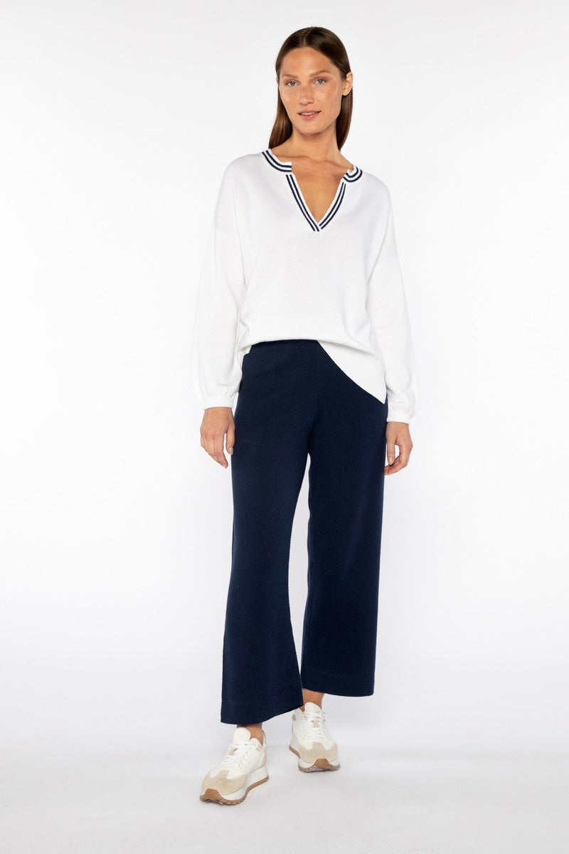 A person is wearing a white V-neck long-sleeve sweater and KINROSS CASHMERE COVERSTITCH SROP COTTON BLEND wide-leg cropped pants. Standing on a white background, the outfit includes white sneakers with beige soles, highlighting a comfortable, casual style.