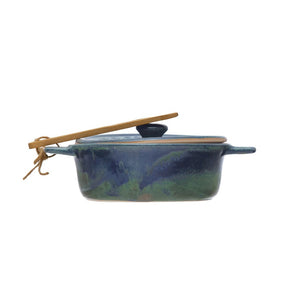 Top view of the CREATIVE COOP BRIE BAKER WITH BAMBOO SPREADER, a round blue stoneware design with lid embossed "Brie Baker Fromage," featuring two handles and accompanied by a small bamboo spreader tied with twine.