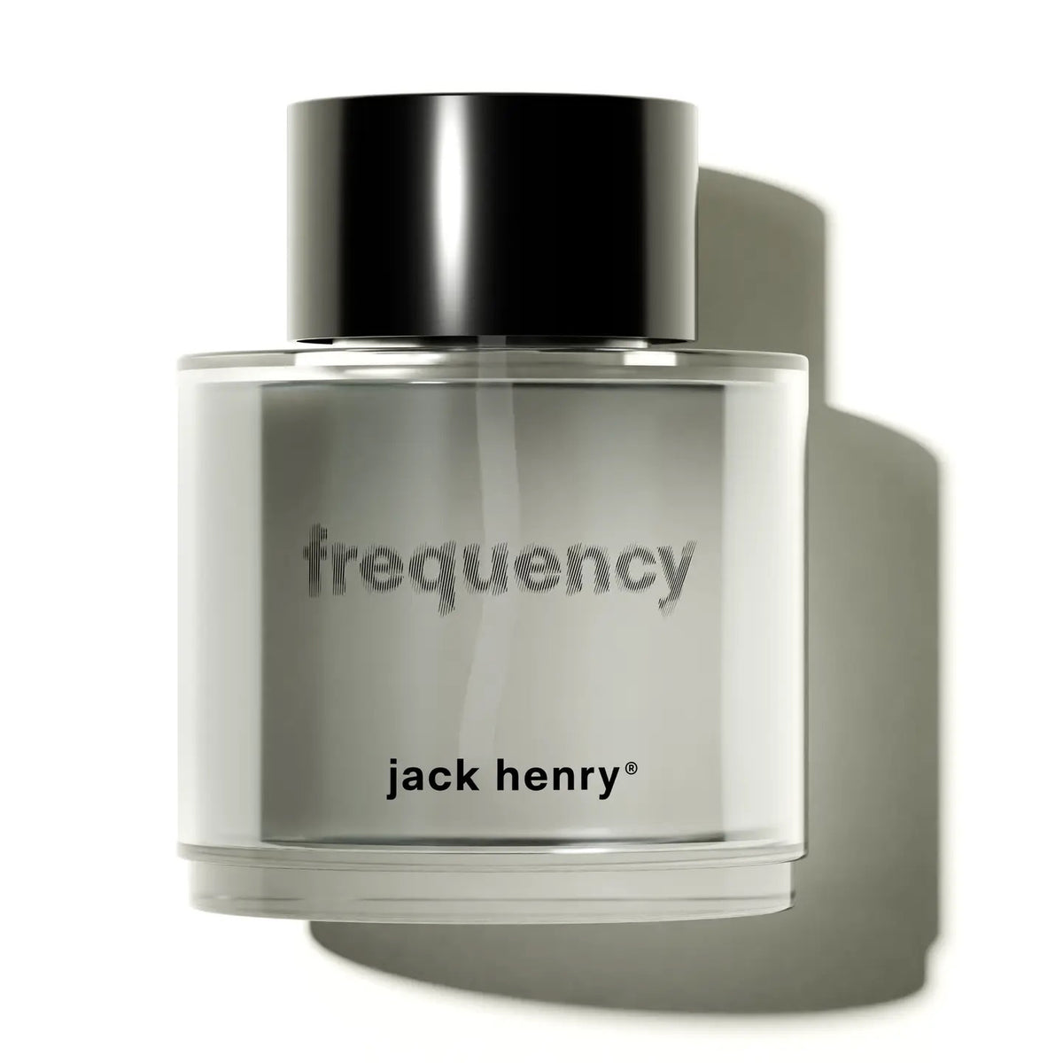 A clear glass bottle of JACK HENRY - FREQUENCY EAU DE PARFUM, with &quot;frequency&quot; and &quot;JACK HENRY&quot; labels and a black cap, sits on white, casting a soft shadow—an elegant, cruelty-free unisex fragrance by JACK HENRY.