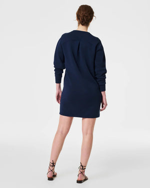 A woman is wearing the SPANX AirEssentials Crew Neck Dress, a black, long-sleeve, knee-length dress from the SPANX brand, with her hands in the functional pockets. She is looking to the side and has long, straight hair. Paired with white sneakers, she stands against a plain white background in this light-as-air fabric attire.