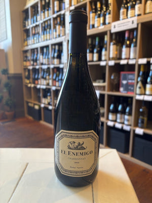 A dark glass wine bottle with a cream label reading "EL ENEMIGO CHARDONNAY 2022" from WINE: WINEBOW features a black foil top. Inspired by Jura, this Valle de Uco Chardonnay stands upright against a plain white background.