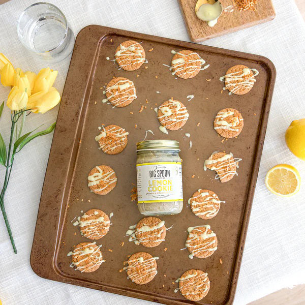 A jar of Big Spoon Roasters Cashew Lemon Coconut Nut Butter sits with a gold lid and a white label adorned with yellow accents. The label features the product name, brand logo, and highlights that this cashew butter is sweetened with coconut nectar and handcrafted from natural ingredients.