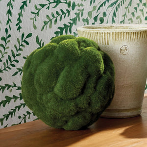 A round, green object resembling a moss-covered sphere is visible against a white background. The surface is textured, giving it a fluffy, organic appearance—perfect for adding a touch of Napa California charm to your home decor with the MOOD MOSS ORB 7" from NAPA HOME AND GARDEN.