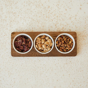 Three small stoneware bowls are placed on a rectangular mango wood tray. The bowls are evenly spaced and aligned in a row. The MANGO WOOD TRAY WITH BOWLS by CREATIVE COOP features a minimalist design with a natural and rustic aesthetic.