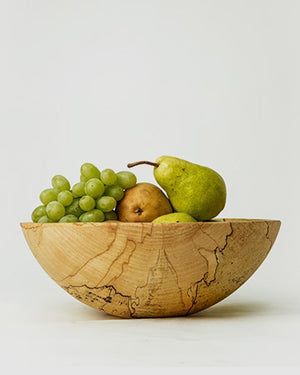 A Classic Round Spalted Maple Bowl 18" from Petermans Boards & Bowls Inc, expertly crafted from upcycled wood, holds a variety of fresh fruits: a bunch of green grapes, a brown pear, and a green pear, displayed against a plain white background.