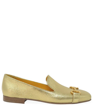 The Madison Maison Square Toe Loafer in gold metallic showcases its handmade craftsmanship and 100% leather composition. This single loafer, characterized by a low wooden heel and square toe, is adorned with a decorative gold buckle on the front. The opulent gold interior lining enhances its luxurious appeal, elegantly displayed in a side profile view against a plain white background.