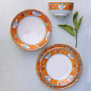 The VIETRI - MELAMINE CAMPAGNA DINNER PLATE by VIETRI features a decorative border with blue and white birds, red tulips, and green leaves on a vibrant orange background. The central section of the plate is plain white, and the border also includes a blue rim, ensuring durability while adding charm to your table.