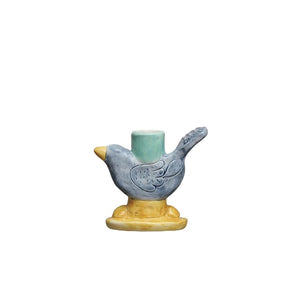 Three minimalist CREATIVE COOP candlesticks display candles; two are HAND PAINTED STONEWARE BIRD TAPER HOLDERS with a navy reactive glaze, and the third features a circular design. Each is uniquely positioned on white blocks against a plain background.