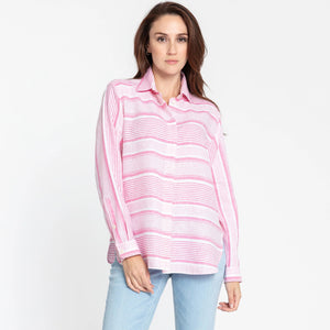 A person with long brown hair is wearing the HINSON WU - GEMMA LONG SLEEVE LINEN SHIRT, which features a light pink and white striped pattern and functional side button details. They have paired it with light blue jeans and are posing against a plain white background, looking directly at the camera with a neutral expression.