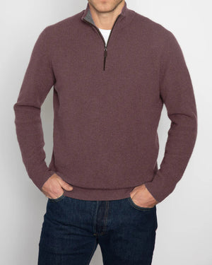 A person wearing a maroon KINROSS CASHMERE - MENS CASHMERE SUEDE TRIM RIB QUARTER ZIP MOCK sweater stands with hands in pockets, paired with dark blue jeans against a plain white background.