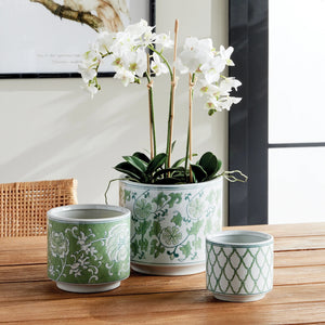 Three NAPA HOME AND GARDEN - IMPERIAL CYLINDER POTs with drainage holes are arranged on a white surface. These handcrafted pieces feature subtle green chinoiserie patterns, varying in size and viewed from above to showcase their unique elegance.