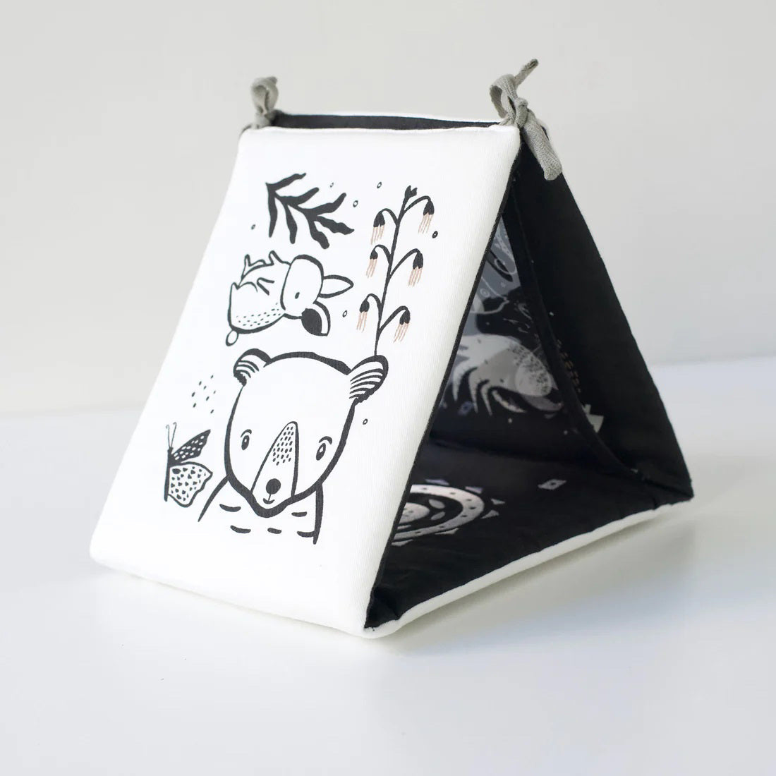 A TUMMY TIME GALLERY soft book from WEE GALLERY, featuring black and white fish and squid illustrations, is partially inserted in a clear front pocket. A brown tag attached by a string reads &quot;tummy time gallery.&quot; This Montessori toy, ideal for sensory development, rests on a plain white surface.