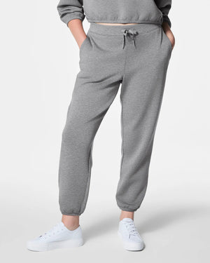 A person in SPANX - AirEssentials Jogger Pant in Heather Gray with a drawcord waist and matching sweatshirt stands with hands in pockets, paired with white sneakers. The luxuriously soft fabric against a plain white background highlights their cozy, relaxed style.