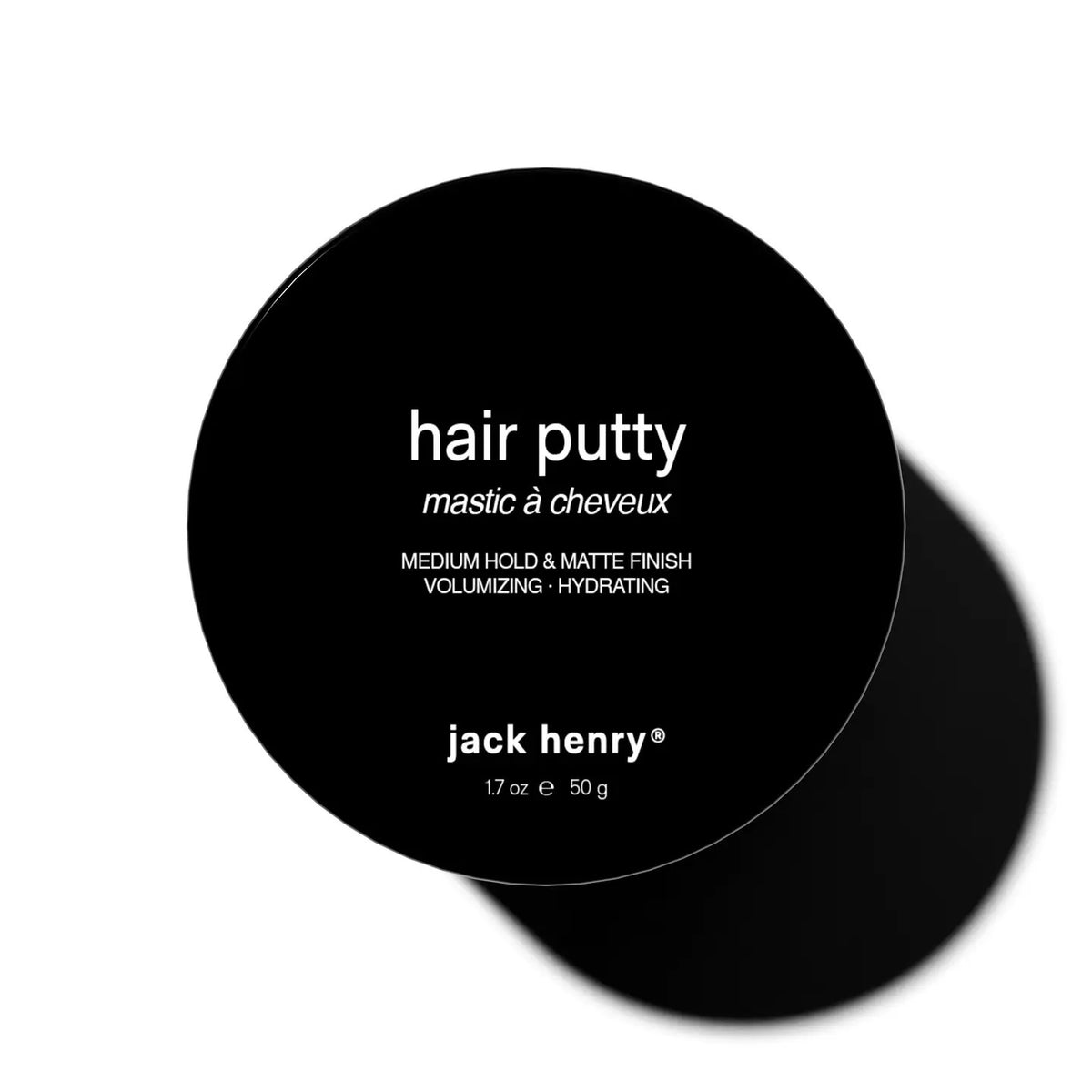 A round black container labeled &quot;JACK HENRY - HAIR PUTTY&quot; features white text promoting hydrating, volumizing benefits with medium hold and a matte finish. The Jack Henry container casts a shadow on a white background.