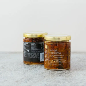 Two jars of Le Bon Magot's Brinjal Eggplant Caponata with Curry Leaves are shown. The jars have gold lids with front labels highlighting the product description and ingredients. One jar is displayed front-facing while the other shows the nutritional information, perfect for savory applications like aubergine relish.