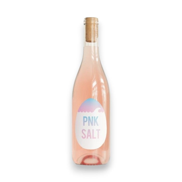 A clear glass bottle with a cork contains pale pink OVUM PNK SALT ROSE by WINE: ADVINTAGE. Its label shows a pink and blue egg with &quot;PNK SALT&quot; in bold, and the Columbia Valley-inspired rosé delivers bracing acidity on a crisp finish.