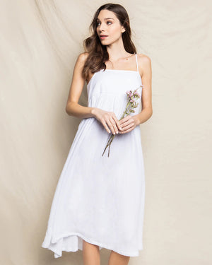 The PETITE PLUME - GAUZE SERENE NIGHT DRESS by PETITE PLUME is a flowing, sleeveless, white cotton gauze sundress with thin spaghetti straps. It features a fitted bodice and a long, airy skirt that reaches down to the ankles, creating an elegant and breezy look ideal for luxury loungewear.