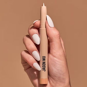 Close-up of a hand with white painted nails holding a sparkle pearl colored eyeshadow pencil with a pink tip, branded with "JASON WU BEAUTY" in black text against a solid neutral beige background.