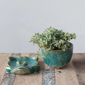 The CREATIVE COOP STONEWARE PLANTER features a green ceramic cup with textured surface, resting on a lounging frog-shaped base. The reactive glaze highlights the frog's limbs, which form part of the support, adding organic charm.