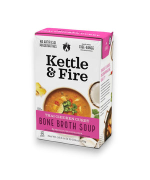 A carton of KETTLE & FIRE - THAI CURRY SOUP is shown. The carton is white with purple accents and features an image of the soup in a bowl, garnished with herbs. It highlights that the bone broth is made from free-range chicken bones and organic ingredients, containing no artificial preservatives.