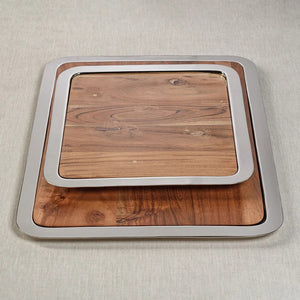 The BRASSERIE STEEL & ACACIA GASTRONOMY BOARD by ZODAX is a rectangular tray featuring a shiny metallic border and a wooden base. The acacia surface shows natural grains and knots, giving it a rustic appearance. With dimensions of 14.25 in x 12.25 in x .75 in, the tray rests on a white background.