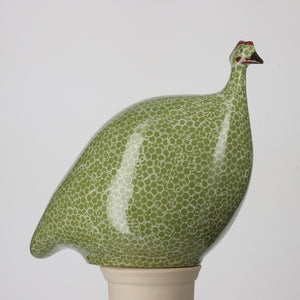 A LES CERAMIQUES DE LUSSAN MEDIUM CERAMIC FRENCH GUINEA IN GREEN SPOTTED WHITE, evoking a Heidi Caillard design. Resembling French guinea hens, the piece is simplistic and stylized, perched on a smooth white base, set against a plain light background.