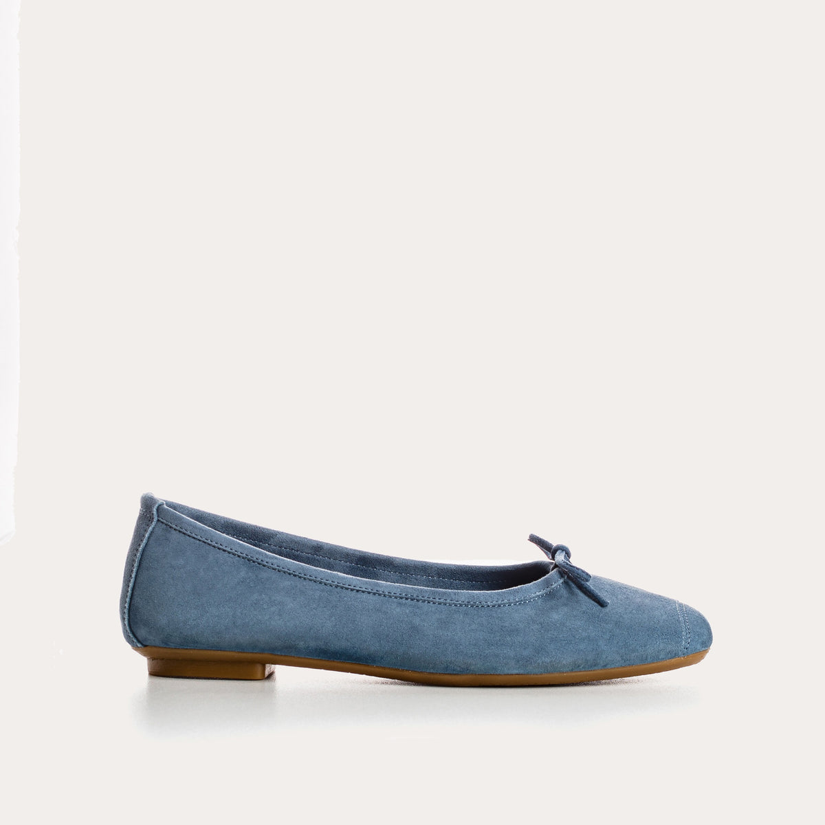The REQINS Harmony Suede Ballerina Flats in Blue Jean feature luxurious goat suede, a delicate front bow, and a low brown heel, displayed on a plain white background.