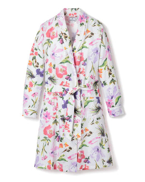 The PETITE PLUME - GARDENS OF GIVERNY ROBE by PETITE PLUME is a white, knee-length robe adorned with vibrant hazy florals in shades of pink, purple, orange, and green. This luxurious sleepwear features a shawl collar and a matching fabric belt tied around the waist, crafted from 100% finest quality cotton.