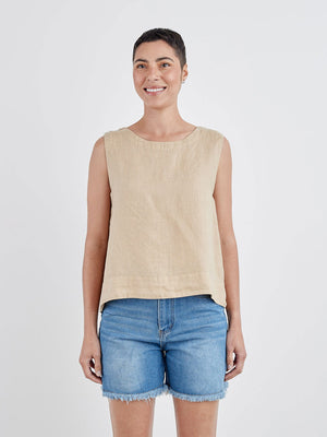 The CUT LOOSE - HI LOW TANK, a sleeveless white linen blouse with a round neckline, is displayed on a white hanger against a light gray wall. Perfect for summer wear, this breathable top by CUT LOOSE features a loose fit and an elegant high-low hem that is shorter in the front and longer in the back.