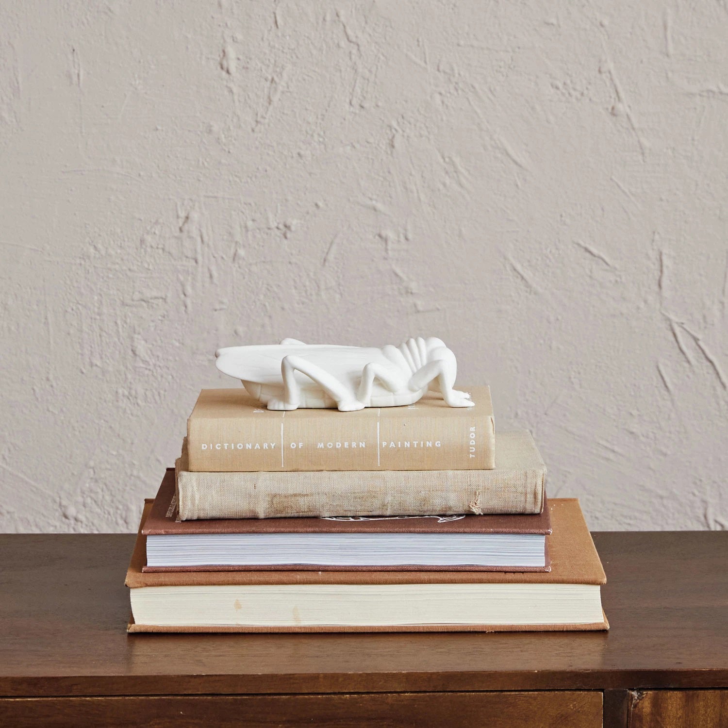 The STONEWARE BISQUE GRASSHOPPER PAPERWEIGHT by CREATIVE COOP features a detailed white stoneware sculpture of a grasshopper, showcasing intricate wings and legs, lying on its side against a plain white backdrop.