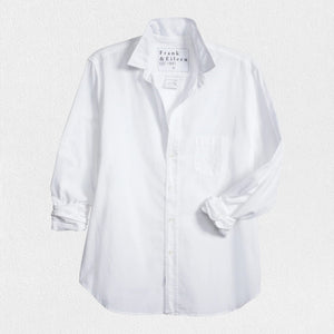 The EILEEN Relaxed Button-Up by Frank & Eileen features a white chambray fabric with long sleeves, a chest pocket, and bust-flattering buttons. The collar displays "Frank & Eileen EST. 1947," while the sleeves are slightly rolled for a casual look.