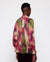 A person with short hair is wearing the MIRTO 1956 Multicolor Chiffon Ikat Print Blouse, a long-sleeve, high-neck top adorned with a vibrant abstract tie-dye pattern in shades of pink, green, and cream. This chiffon blouse by MIRTO 1956 features smocked cuffs on its raglan puff sleeves. The person is shown from the back against a plain white background.