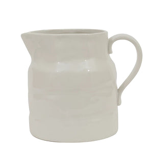 The STONEWARE VINTAGE PITCHER by CREATIVE COOP is a white ceramic piece with a smooth, wavy texture and curved handle, ideal for serving drinks or displaying flowers. It blends minimalist design with vintage-inspired charm.